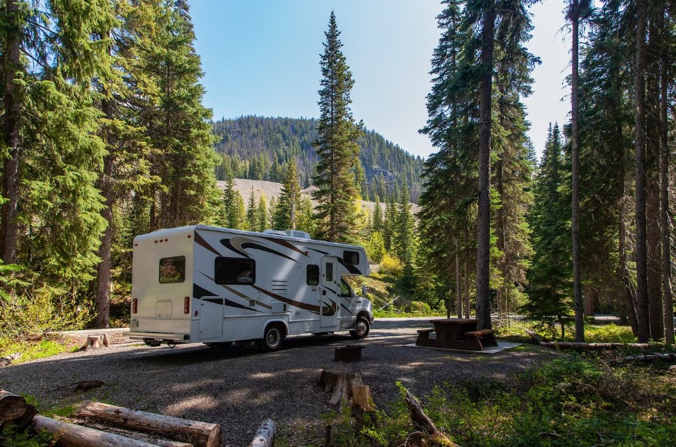 a beautiful campsite in the mountains with an RV and a wooden bench