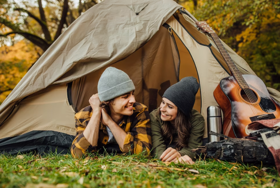 a couple lying in the tent and looking at each other, guitar, thermos outside on the grass